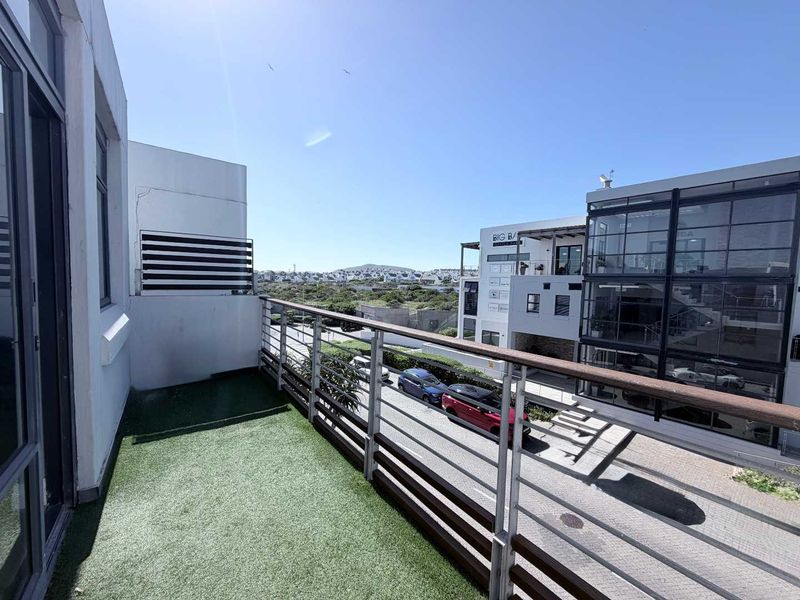 A private balcony featuring artificial turf flooring and a modern metal railing, offering an elevated view of the surrounding neighborhood.