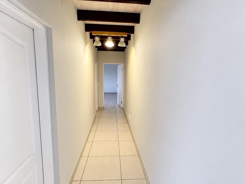 A bright, clean hallway featuring neutral tiled flooring and decorative exposed timber ceiling beams with integrated lighting.