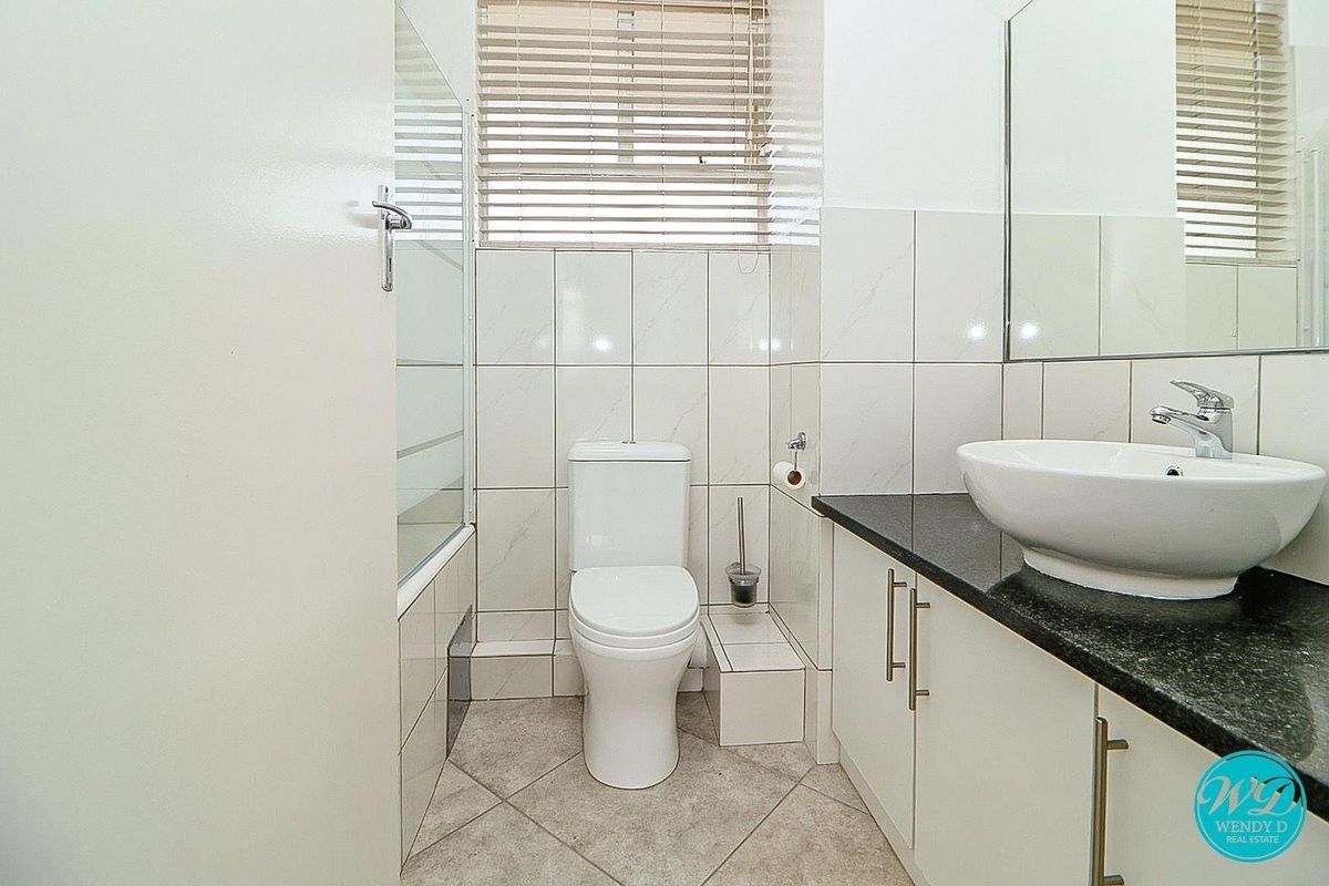 A clean, modern bathroom featuring a white vanity with a black countertop, vessel sink, toilet, and a shower-over-bath combination with tiled walls.
