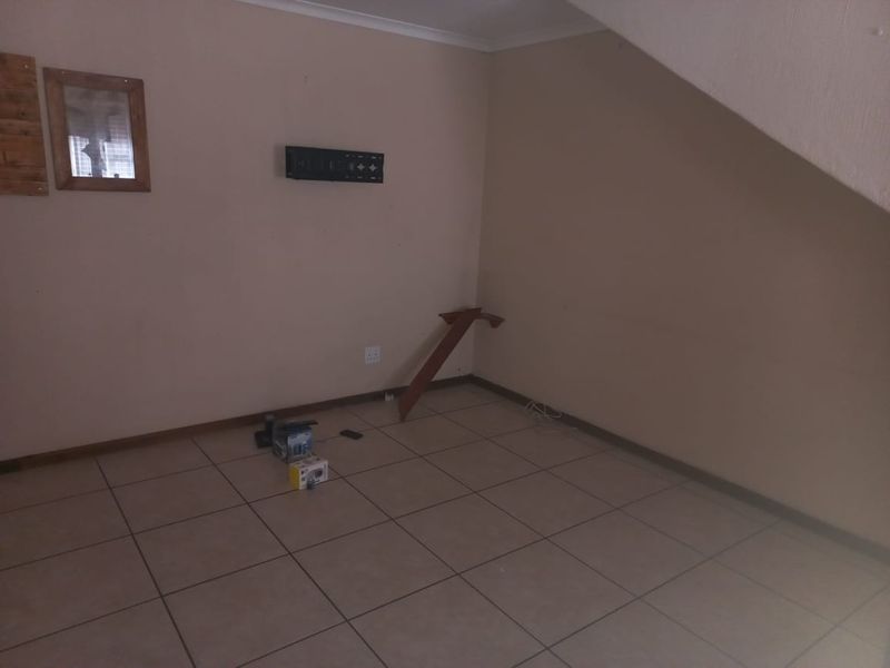 An empty living area featuring ceramic floor tiles and neutral wall finishes, located under a staircase with coved ceiling cornicing.
