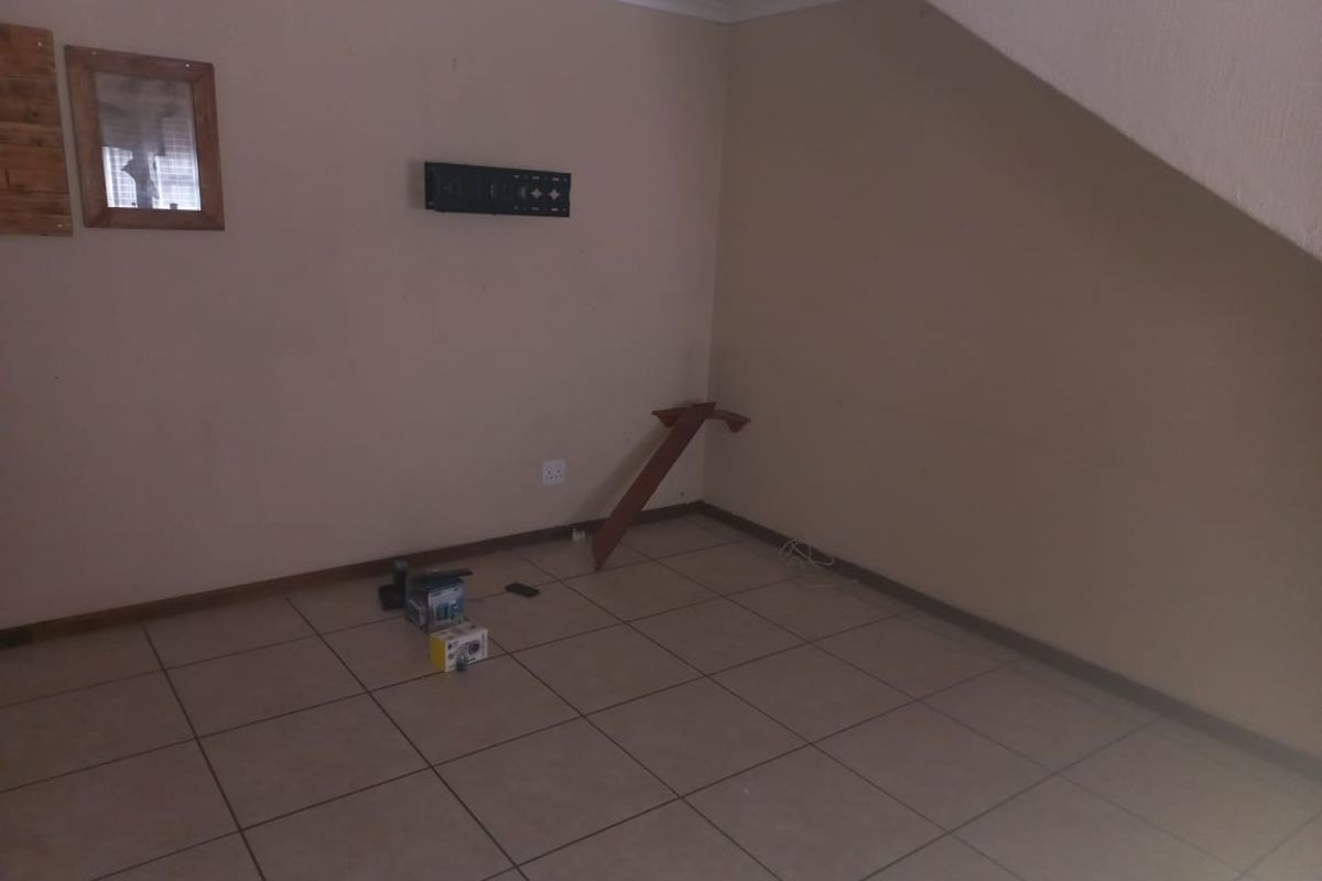 An empty living area featuring ceramic floor tiles and neutral wall finishes, located under a staircase with coved ceiling cornicing.