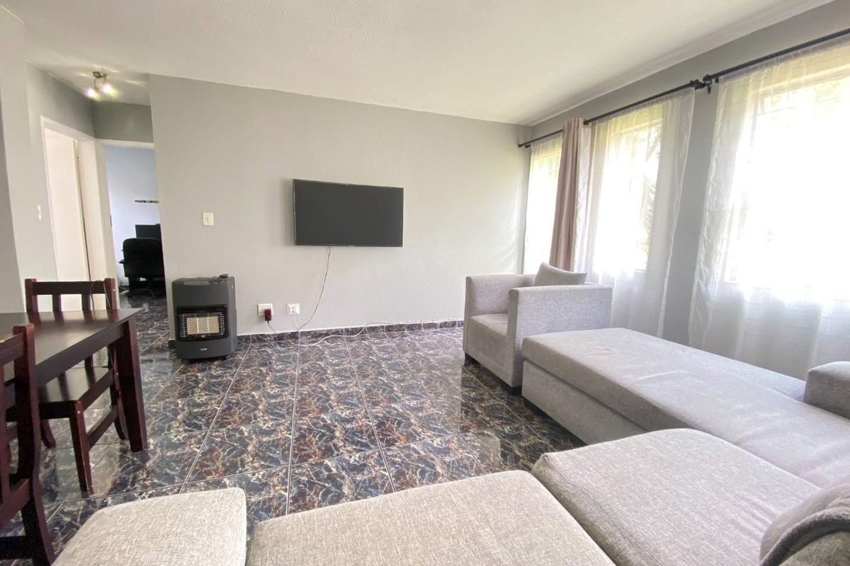 A living room featuring dark marble-effect floor tiles, neutral wall paint, and large windows allowing for natural light.