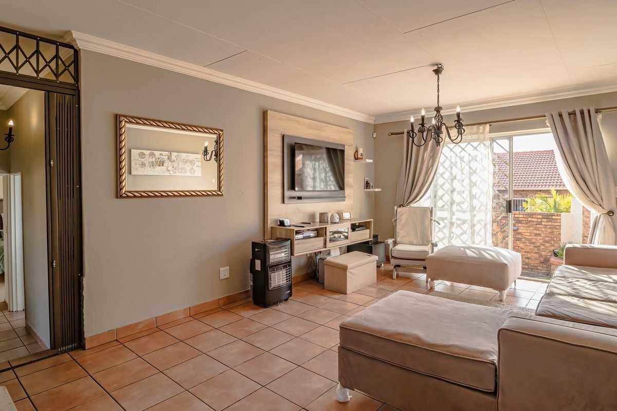 A well-maintained living room featuring tiled flooring, crown molding, and a built-in media unit, with direct access to an outdoor patio area.