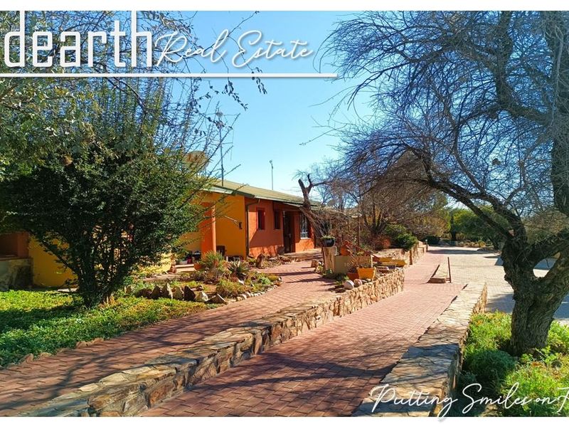 Front exterior view of a retirement village unit featuring a brick paved driveway, stone retaining walls, and established garden landscaping.