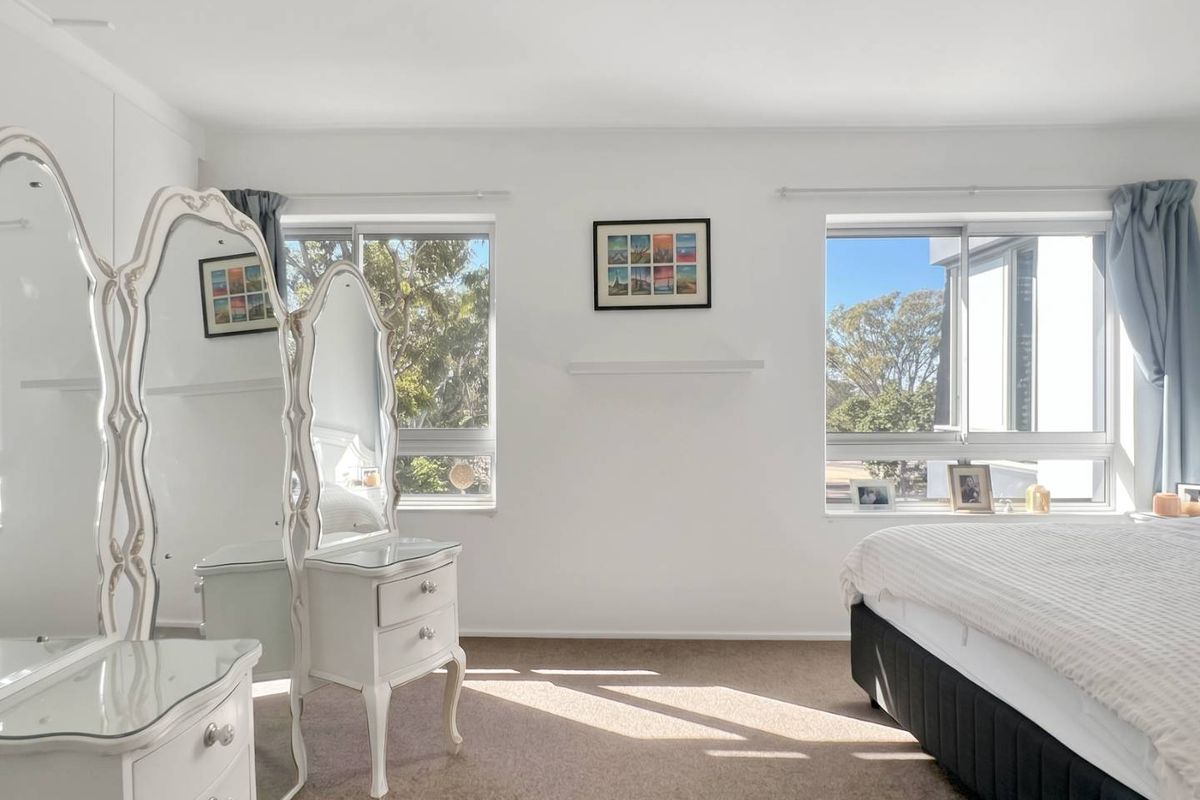A bright and spacious bedroom featuring neutral carpet flooring, dual sliding windows providing natural light, and a central ceiling light fixture.