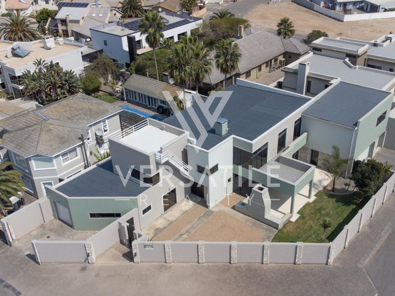 Aerial view of a modern multi-level residential property featuring a metal roof, perimeter wall, and paved driveway in a suburban neighborhood.