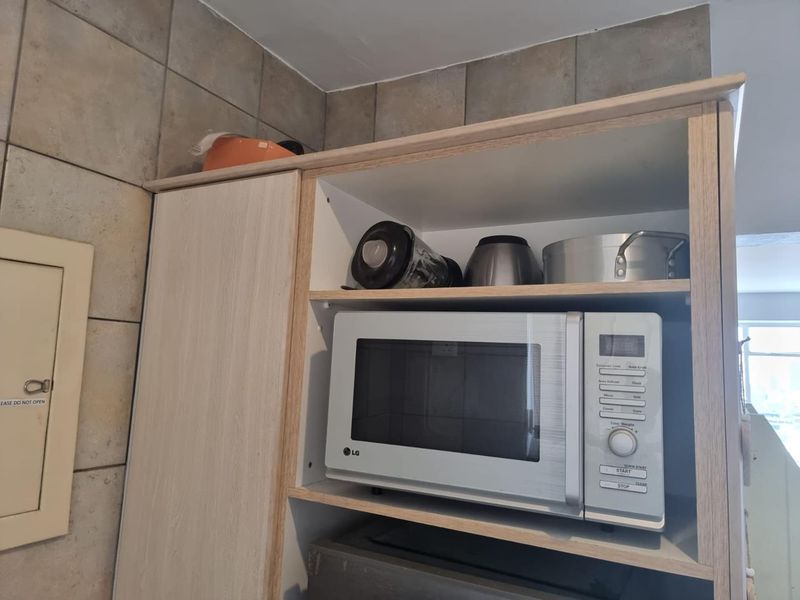A close-up view of kitchen cabinetry featuring a dedicated microwave shelf and tiled backsplash.