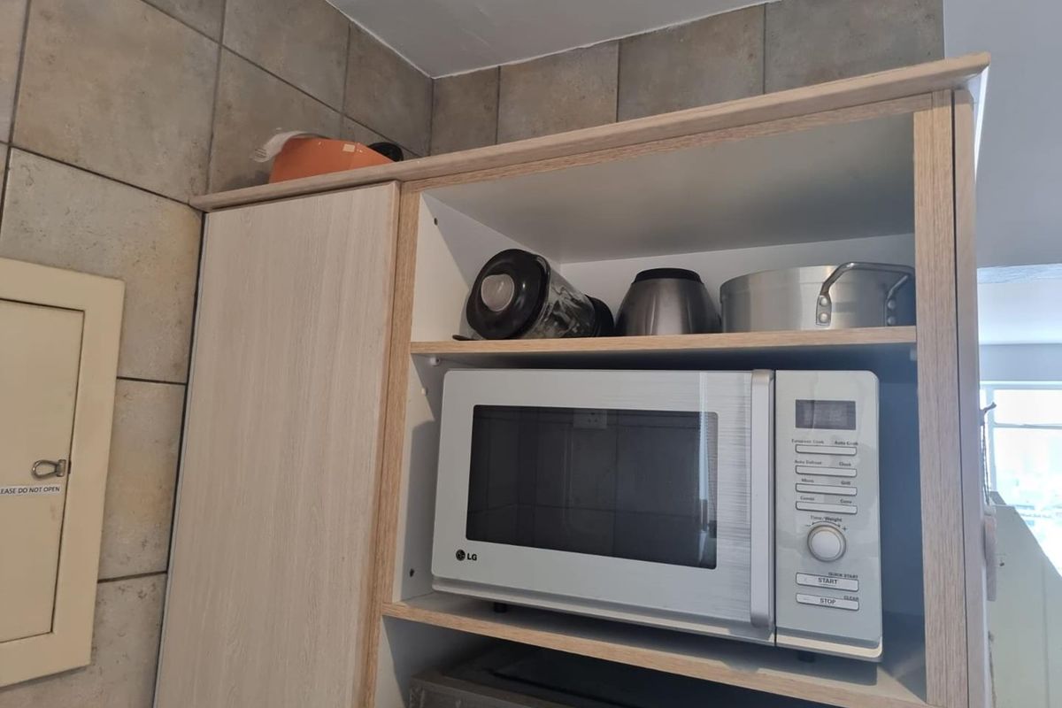A close-up view of kitchen cabinetry featuring a dedicated microwave shelf and tiled backsplash.