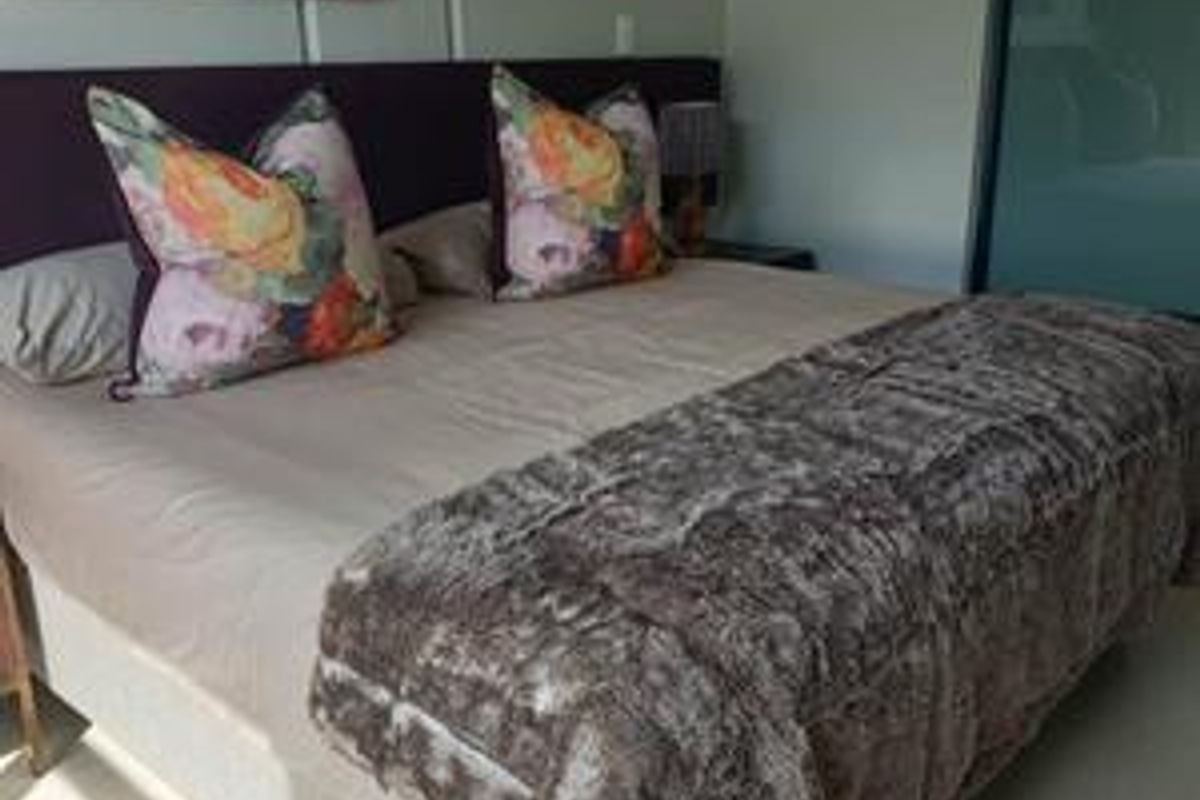 A comfortable bedroom featuring a built-in headboard and a sliding door wardrobe, providing functional storage and a clean aesthetic.