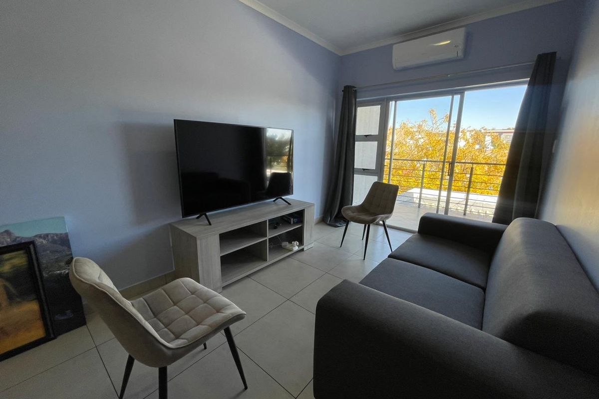 A bright living room featuring tiled flooring, a wall-mounted air conditioning unit, and large sliding glass doors leading to a balcony.