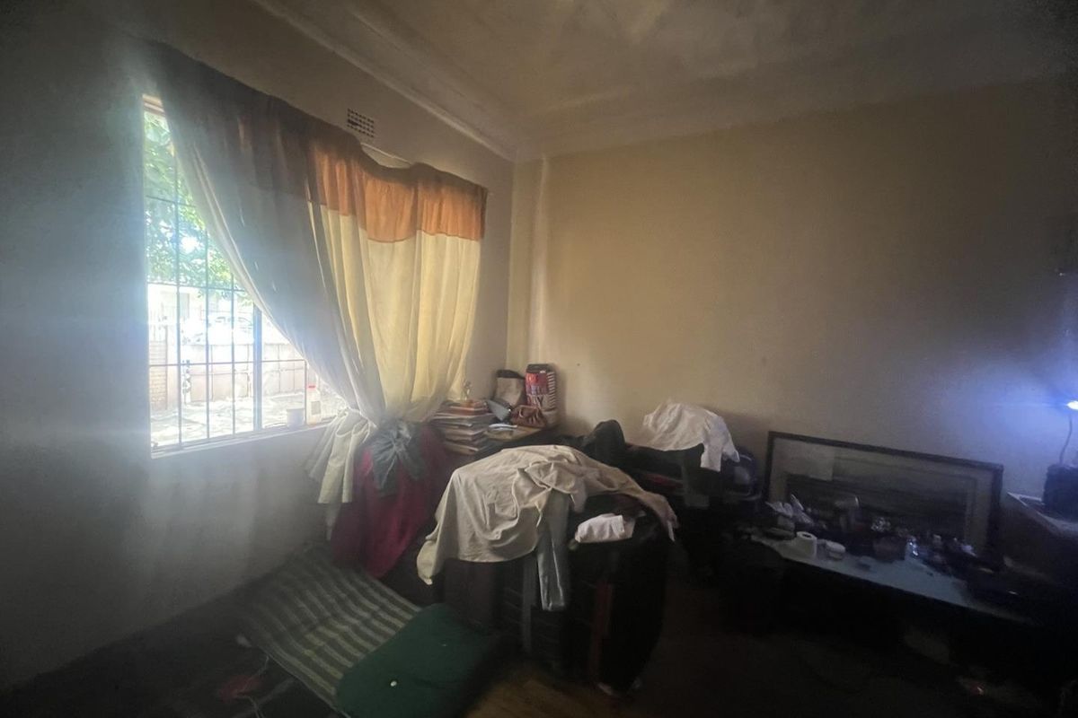 A bedroom featuring a large window with security bars, original flooring, and a ceiling showing signs of wear.