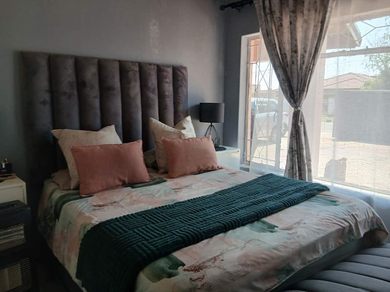 A bedroom featuring a large upholstered headboard and a window fitted with security bars, allowing natural light into the space.