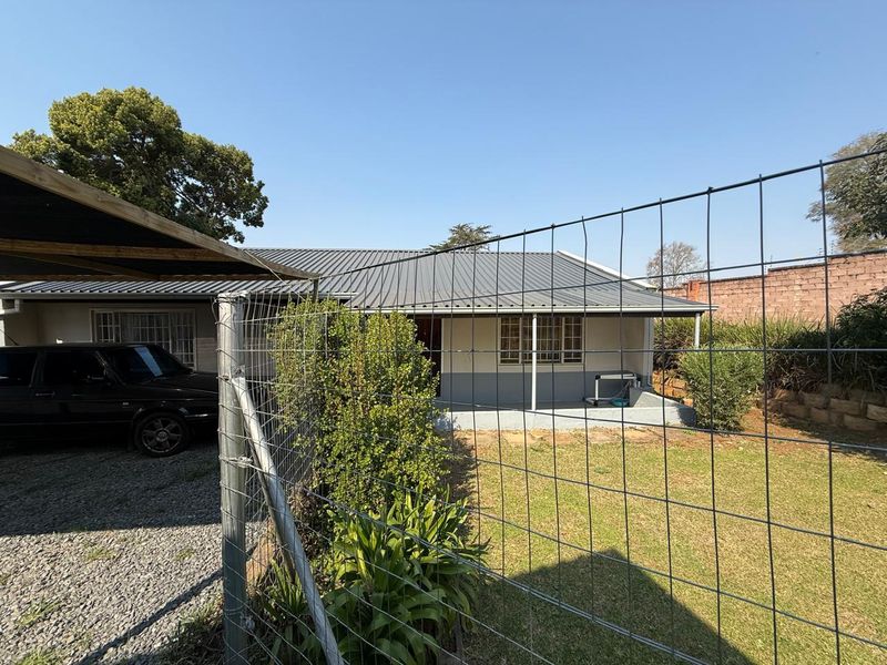 Front exterior view of the property featuring a metal roof, concrete patio area, gravel driveway, and secure perimeter fencing.