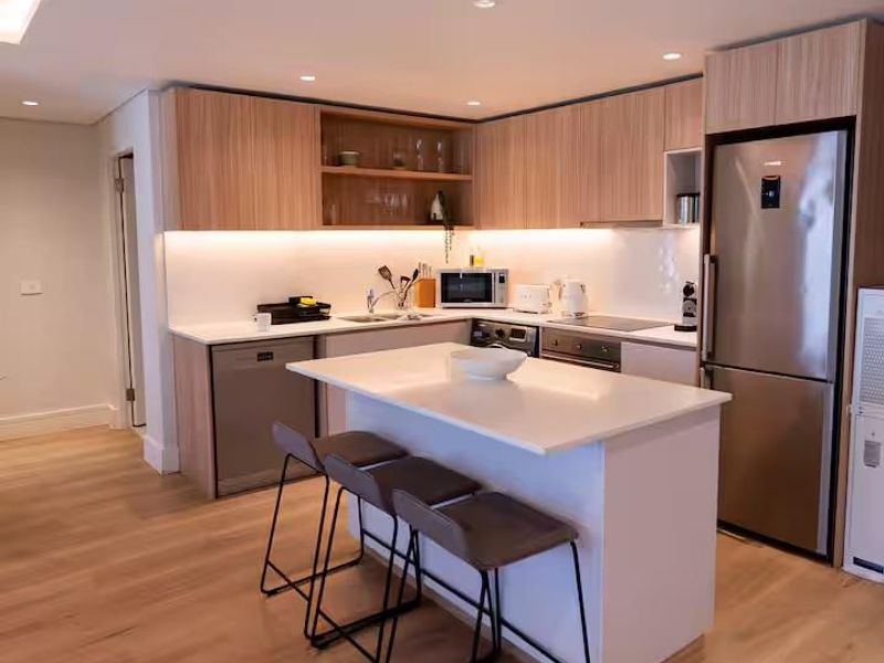 Modern kitchen featuring light wood cabinetry, stone countertops, a central island with breakfast bar seating, and integrated stainless steel appliances.