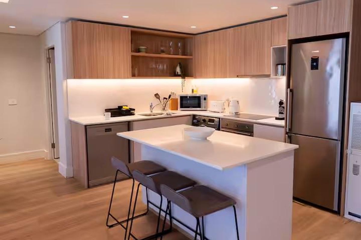 Modern kitchen featuring light wood cabinetry, stone countertops, a central island with breakfast bar seating, and integrated stainless steel appliances.