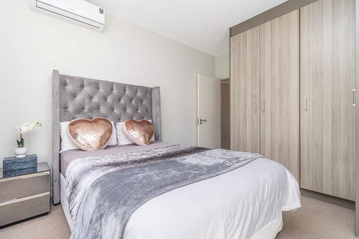 A well-maintained bedroom featuring neutral carpeted flooring, ample built-in cupboard storage, and a wall-mounted split-system air conditioning unit.