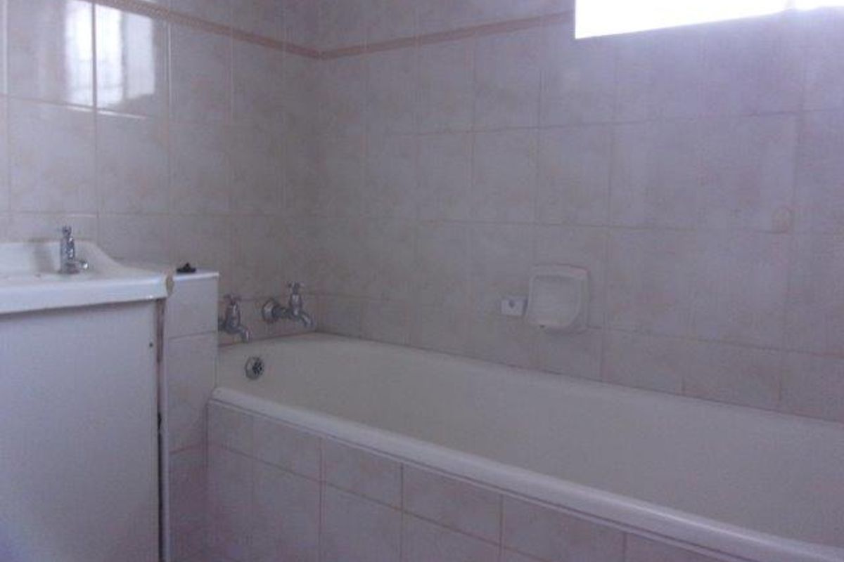 A functional bathroom featuring a standard bathtub, wall-mounted basin, and tiled wall finishes.
