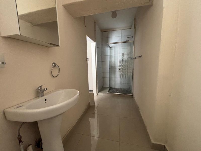 A functional bathroom featuring a pedestal washbasin, a glass shower enclosure, and tiled flooring, requiring cosmetic updates to improve its overall condition.