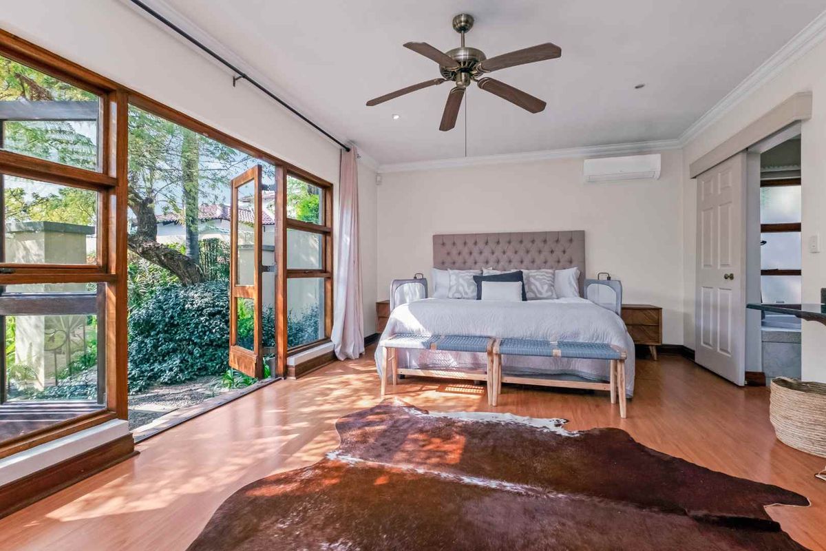 Spacious bedroom featuring large timber-framed glass doors opening to the garden, a ceiling fan, and a wall-mounted air conditioning unit.