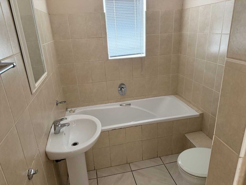 A functional bathroom featuring a pedestal basin, built-in bathtub, and toilet, finished with neutral wall and floor tiling.