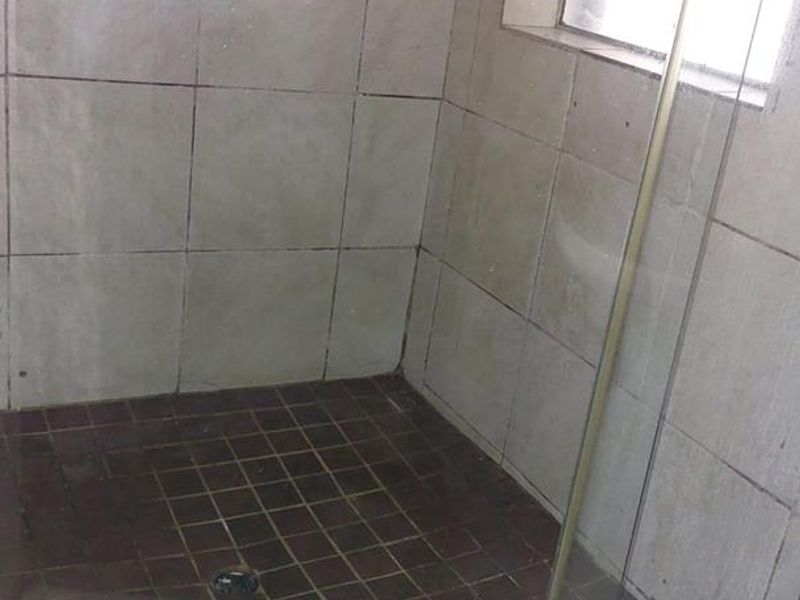 A walk-in shower enclosure featuring dark tiled flooring and wall accents, requiring maintenance to the grout and tile surfaces.