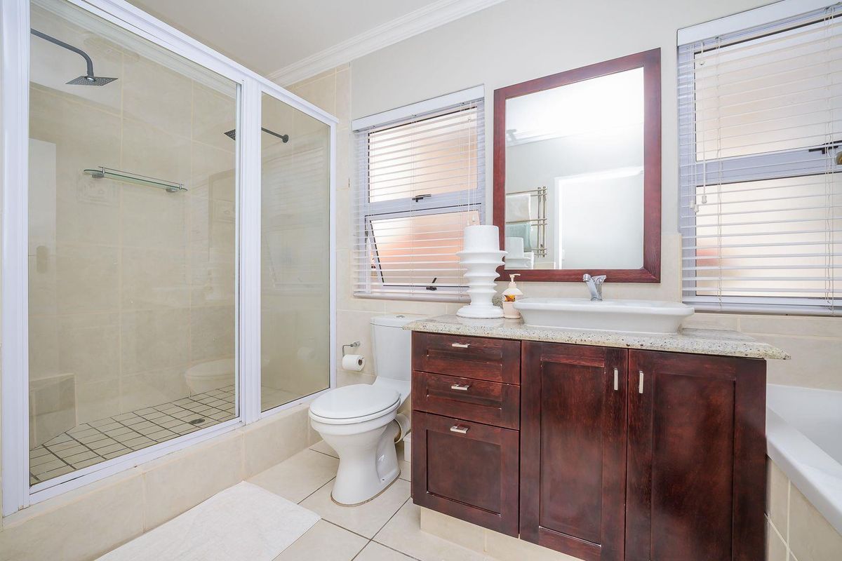 A well-maintained bathroom featuring a glass-enclosed shower, a vanity with a vessel sink, and a toilet, finished with neutral floor and wall tiles.