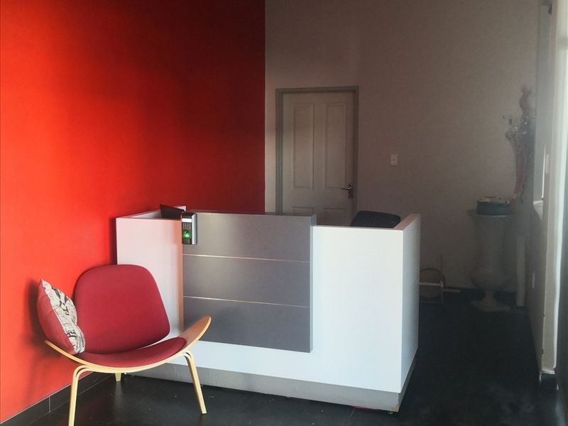 A functional office reception area featuring a built-in desk with integrated access control, tiled flooring, and a bold red accent wall.