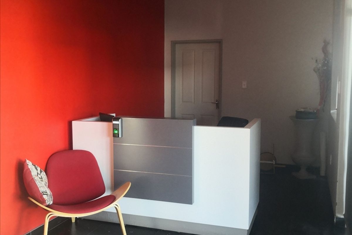 A functional office reception area featuring a built-in desk with integrated access control, tiled flooring, and a bold red accent wall.