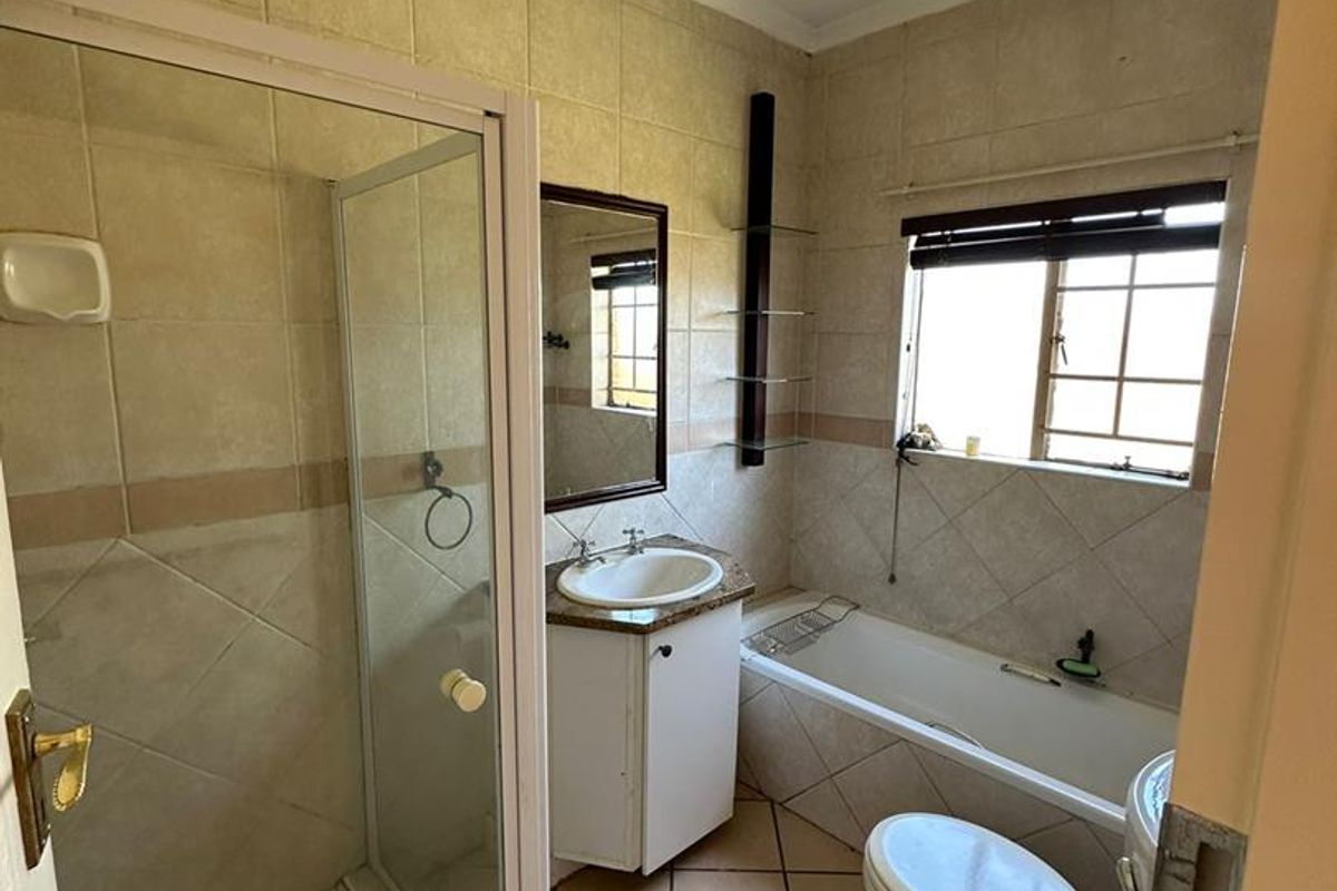 A functional bathroom featuring a shower enclosure, bathtub, vanity basin, and toilet, finished with neutral wall and floor tiling.
