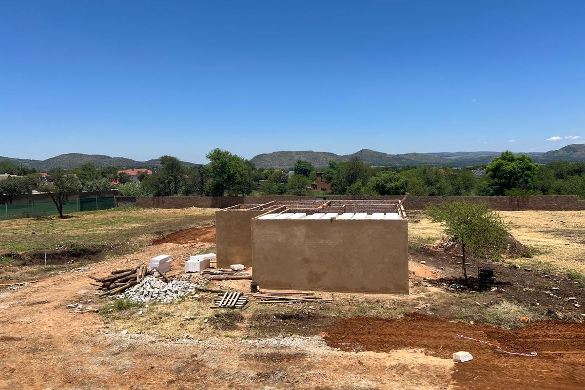An aerial view of a property under construction, showing the initial shell and foundation work on a large, undeveloped plot of land.