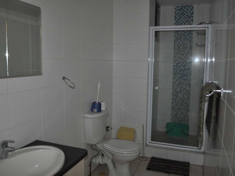 A functional bathroom featuring a shower enclosure with mosaic tile accents, a vanity basin, and a standard toilet with white wall tiling.