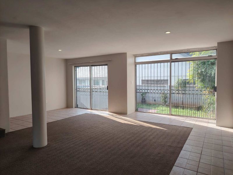 Spacious, empty living area featuring a structural column, tiled and carpeted flooring, and large sliding glass doors with security bars leading to the garden.