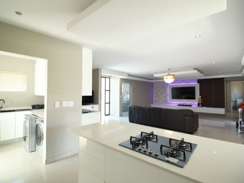 Modern open-plan living area featuring a sleek kitchen with gas hob, quartz countertops, and a sophisticated lounge with integrated feature wall lighting.