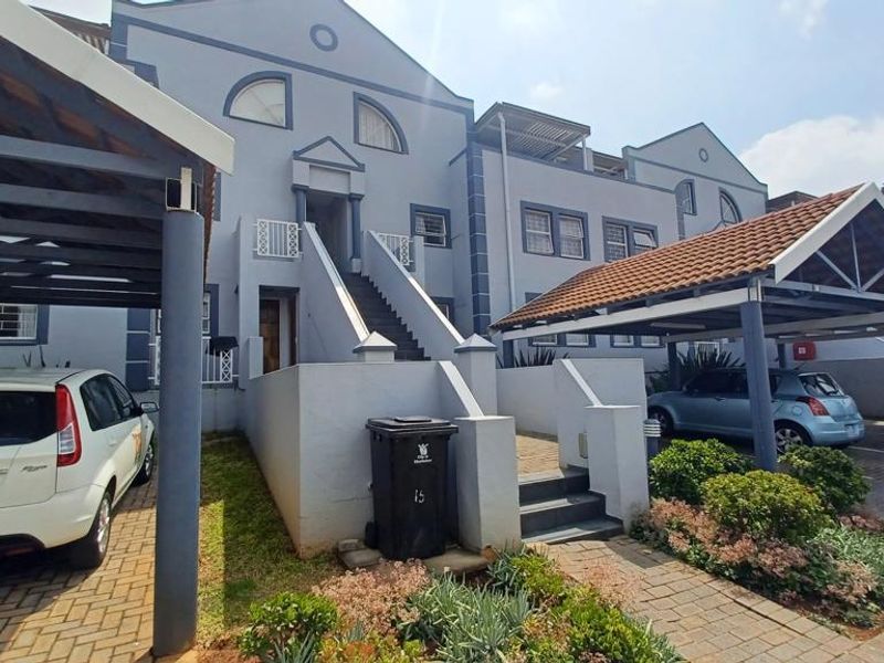 Front elevation of an apartment complex featuring covered parking bays, paved driveway, and external staircase access to upper units.
