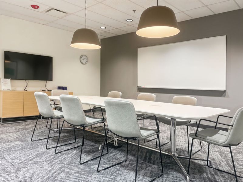 A modern, well-lit office meeting room featuring a large conference table, wall-mounted whiteboard, and professional suspended ceiling finishes.