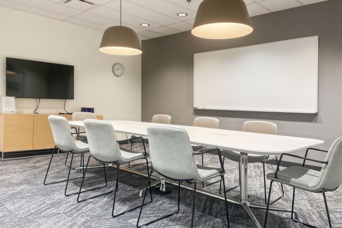 A modern, well-lit office meeting room featuring a large conference table, wall-mounted whiteboard, and professional suspended ceiling finishes.