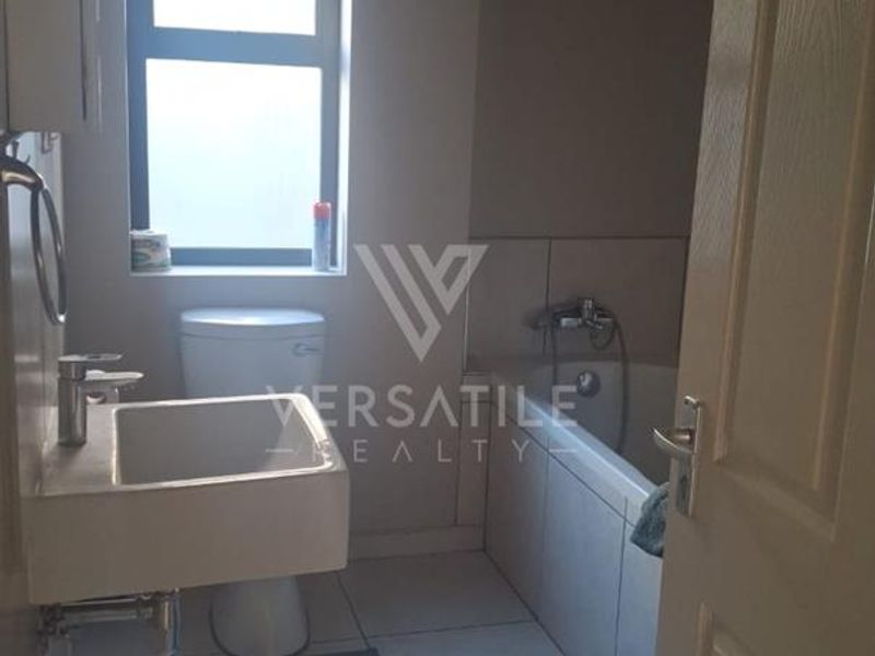 A functional bathroom featuring a wall-mounted basin, toilet, and bathtub with tiled flooring and neutral wall finishes.