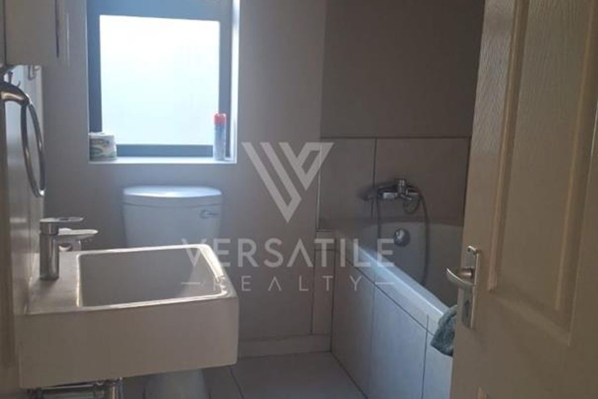 A functional bathroom featuring a wall-mounted basin, toilet, and bathtub with tiled flooring and neutral wall finishes.