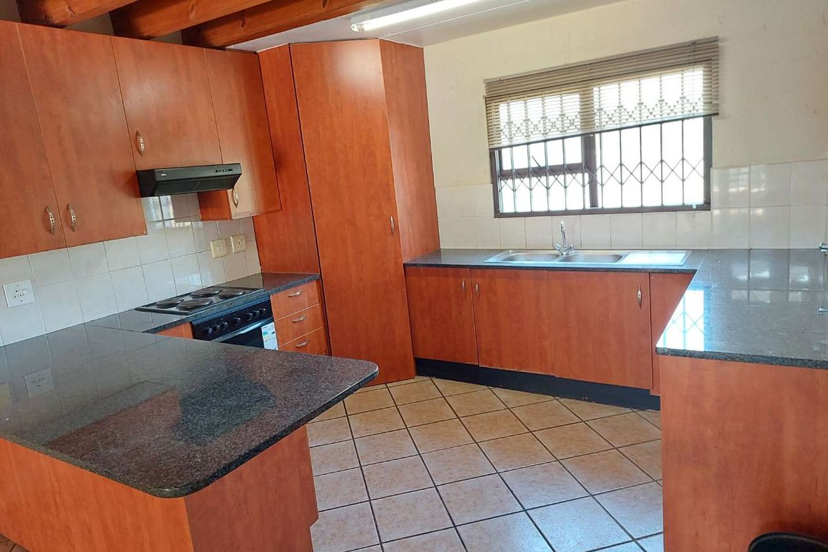 A functional kitchen featuring laminate cabinetry, granite countertops, built-in oven and hob, and exposed timber ceiling beams.