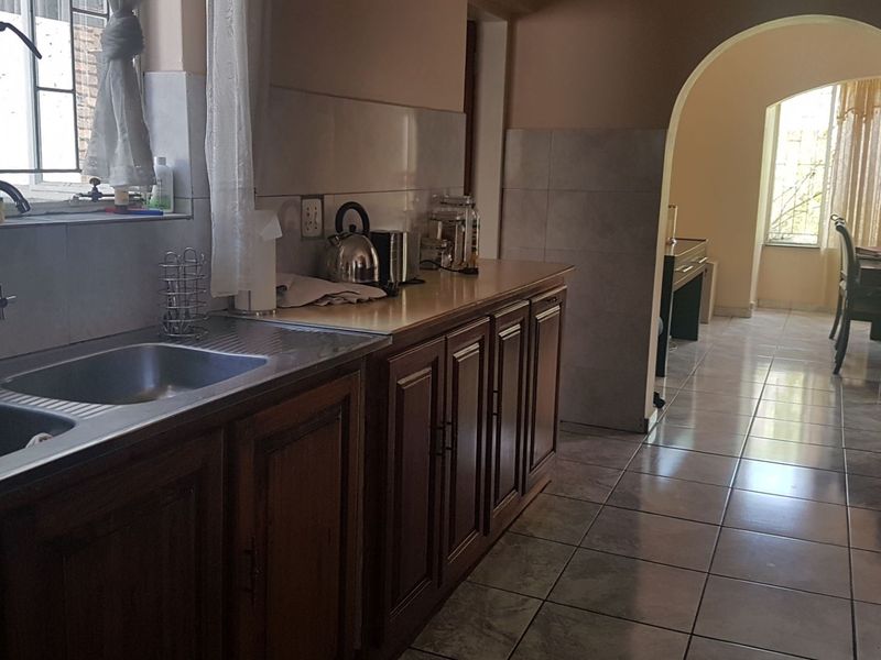 A functional kitchen featuring wooden cabinetry, laminate countertops, and a double basin sink, leading through an arched doorway into the dining area.