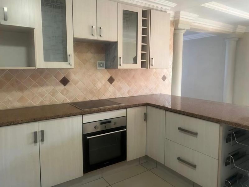 A functional kitchen featuring light-toned cabinetry, granite countertops, a built-in oven, and a tiled backsplash, complemented by decorative architectural columns.