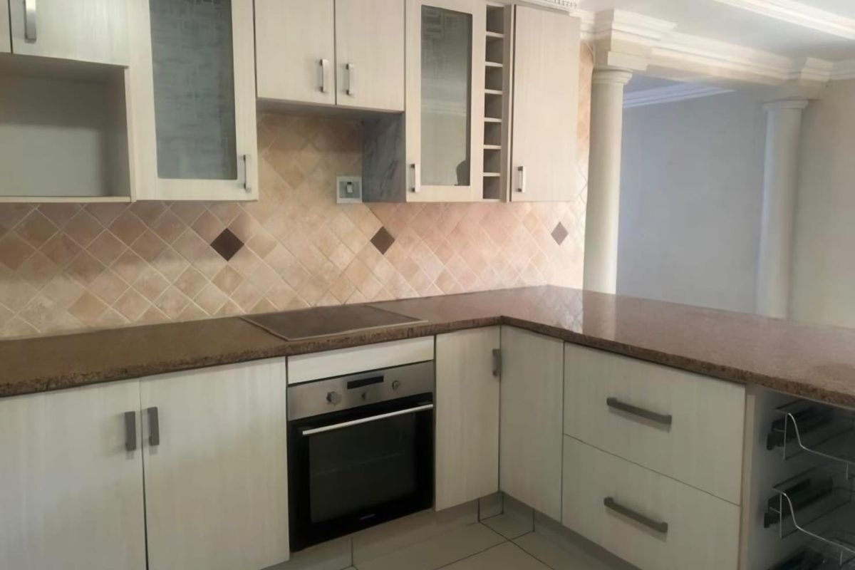 A functional kitchen featuring light-toned cabinetry, granite countertops, a built-in oven, and a tiled backsplash, complemented by decorative architectural columns.