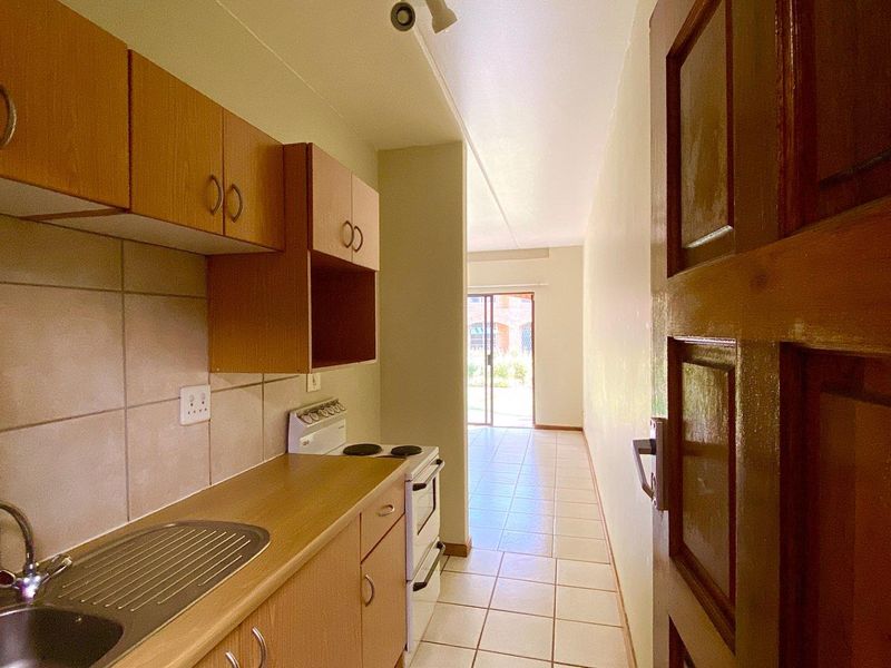 A compact kitchen featuring laminate cabinetry, a stainless steel sink, tiled backsplash, and a freestanding stove, leading towards an open living area.