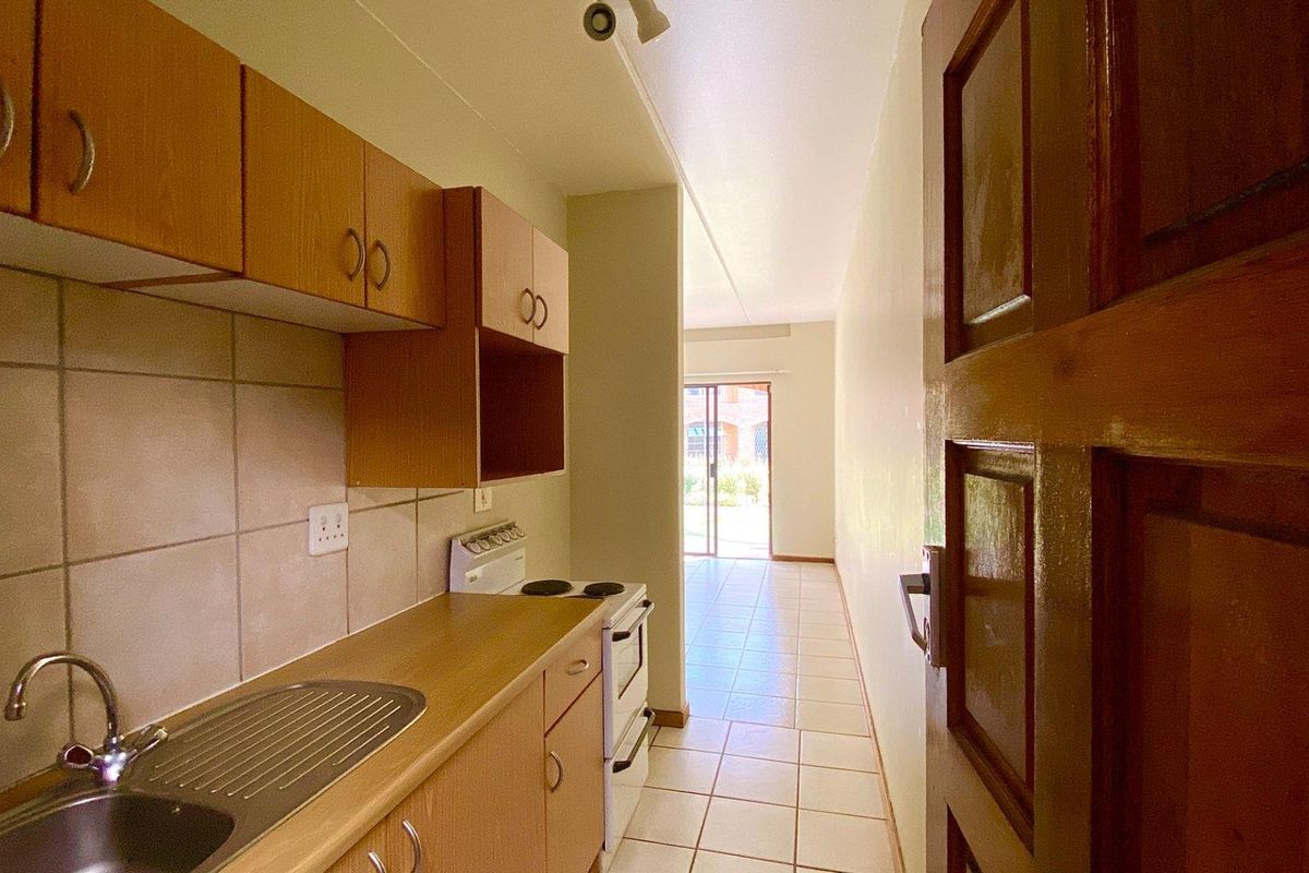 A compact kitchen featuring laminate cabinetry, a stainless steel sink, tiled backsplash, and a freestanding stove, leading towards an open living area.