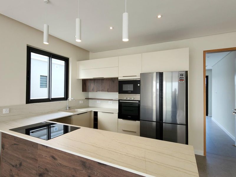 Modern kitchen featuring sleek two-tone cabinetry, stone countertops, integrated appliances, and a functional breakfast bar layout with contemporary pendant lighting.