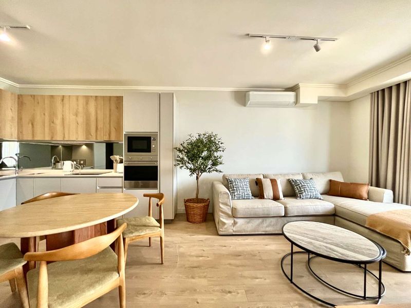 Modern open-plan living area featuring a contemporary kitchen with integrated appliances, light wood-tone cabinetry, and a split-system air conditioner.