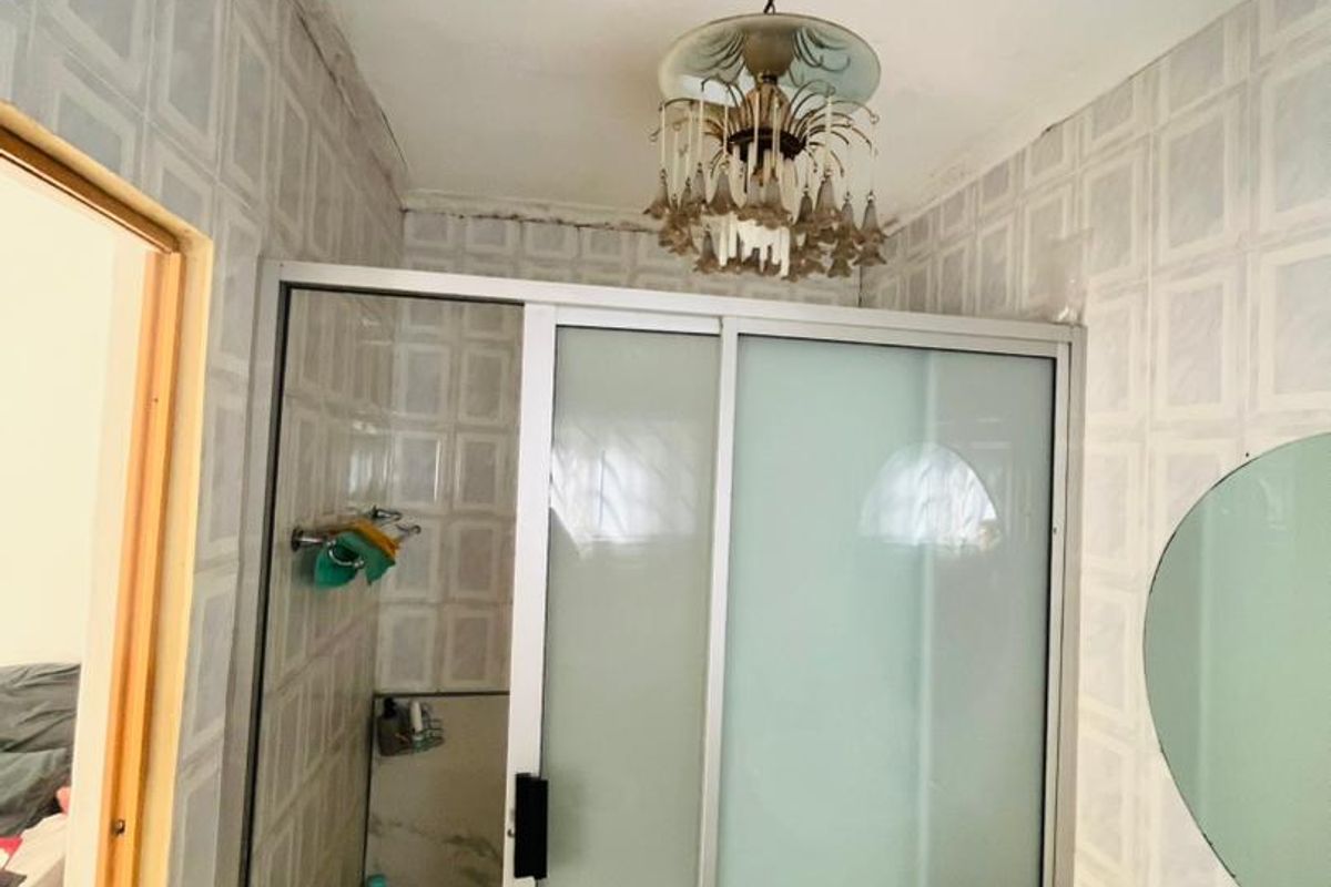 A dated bathroom featuring a shower enclosure, pedestal basin, and tiled finishes, requiring cosmetic updates to modernize the space.