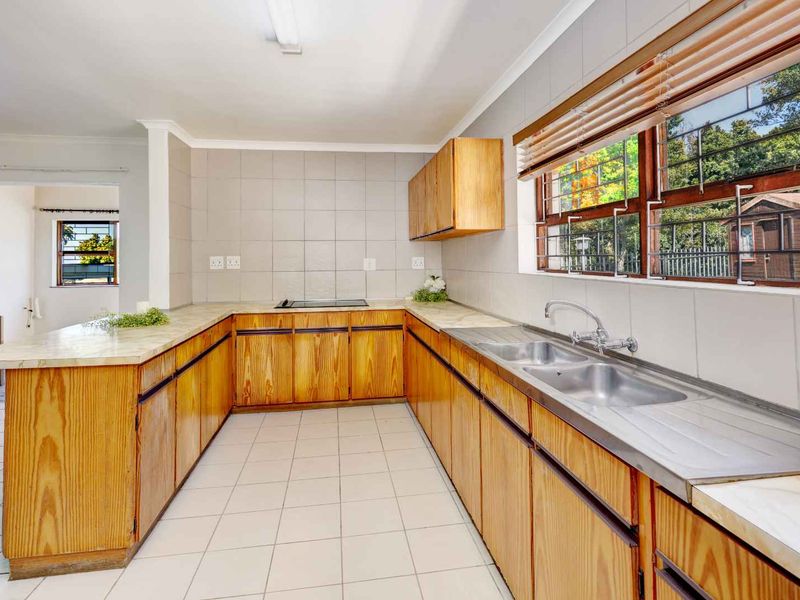 A functional kitchen featuring wooden cabinetry, laminate countertops, a double stainless steel sink, and a built-in electric hob with tiled splashbacks.