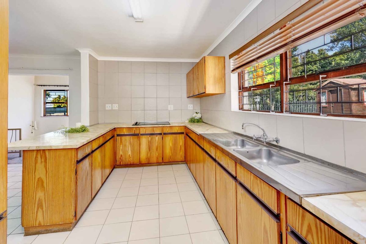 A functional kitchen featuring wooden cabinetry, laminate countertops, a double stainless steel sink, and a built-in electric hob with tiled splashbacks.