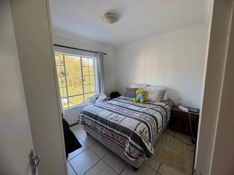 A functional bedroom featuring tiled flooring and a large window that provides natural light and a view of the surrounding greenery.